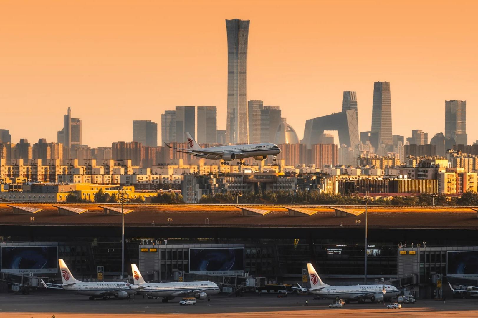 Golden hour view of Beijing airport with city CBD skyscraper skyline, commercial airplane landing