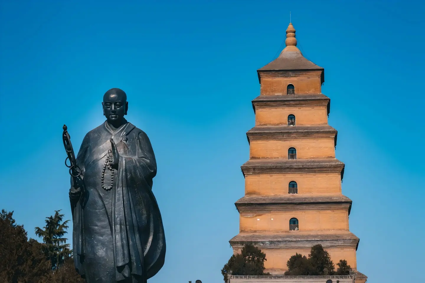 Statue of Xuanzang beside the historic Giant Wild Goose Pagoda under clear blue sky, Xi'an