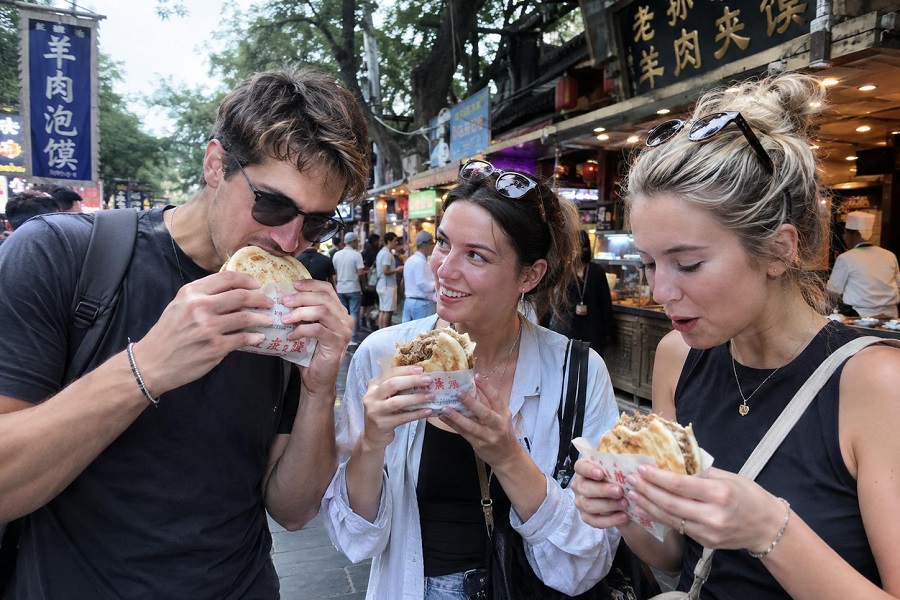 International travelers taste Chinese roujiamo meat buns at Xi'an Muslim Quarter food market