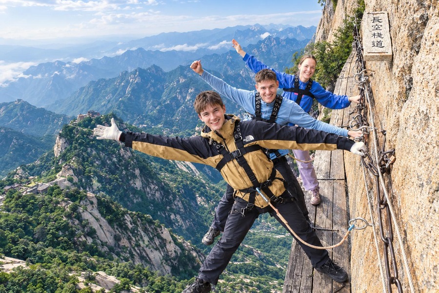 Three foreign tourists with safety harness posing on Huashan dangerous Plank Road in the Sky