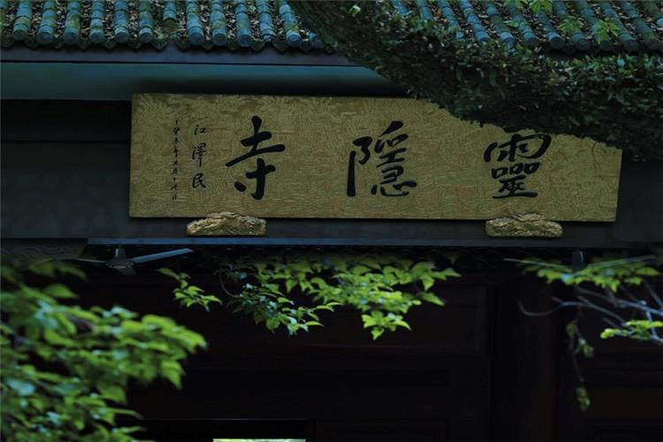 Golden calligraphy plaque of Lingyin Temple framed by fresh green leaves at the temple entrance