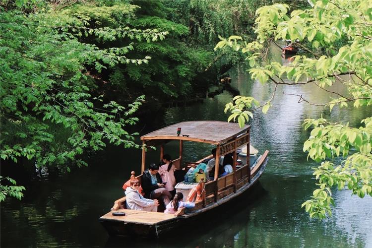 Tourists sightseeing on traditional wooden boat surrounded by lush green foliage in Hangzhou