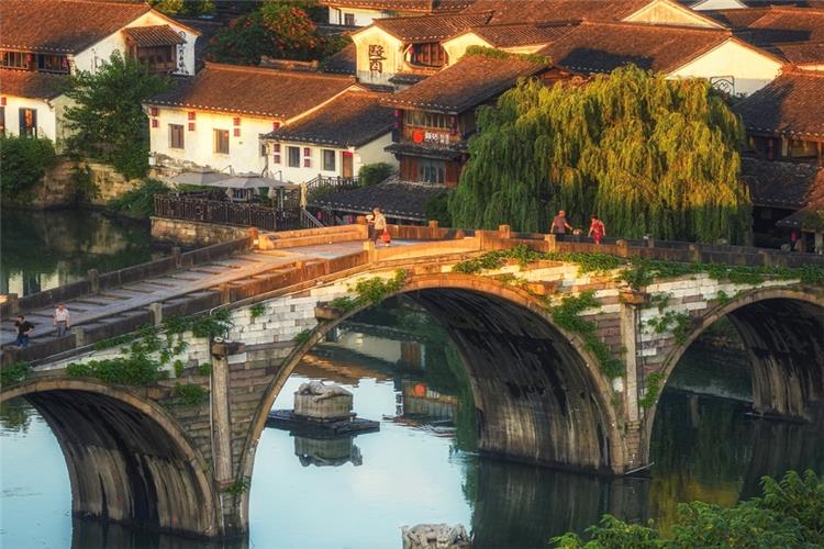 Historic Gongchen Bridge over Grand Canal Ancient Water Town Three-arched ancient stone Gongchen Bridge crossing the Grand Canal, traditional white-washed old houses and weeping willows under warm sunset light in Hangzhou