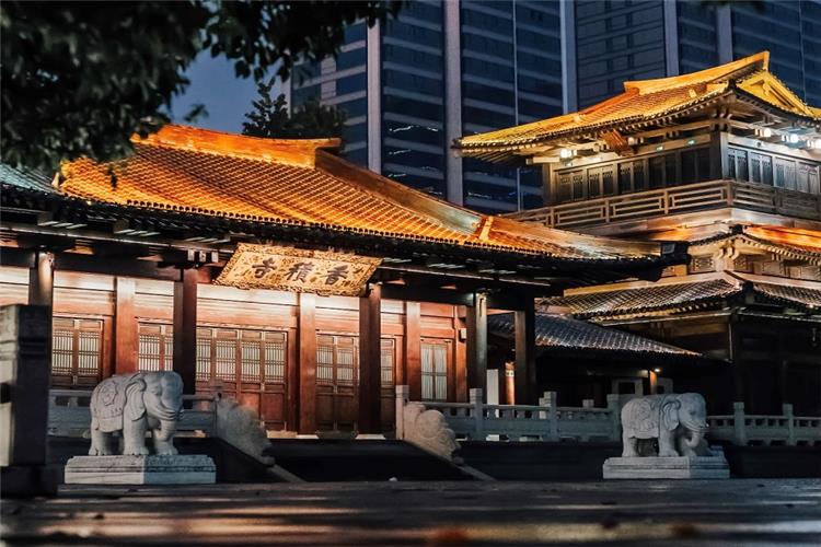 Illuminated Xiangji Temple at Night Lit ancient wooden halls of Xiangji Temple with stone elephant sculptures at the gate, classic Chinese Buddhist architecture against modern city buildings at dusk
