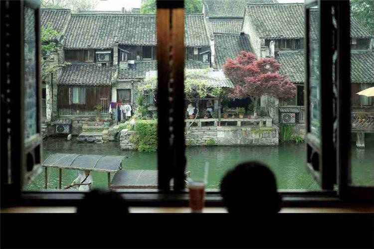 Quiet Canal View Inside Wuzhen Xizha Traditional Jiangnan water town scenery viewed through wooden window, ancient houses and calm canal in Wuzhen