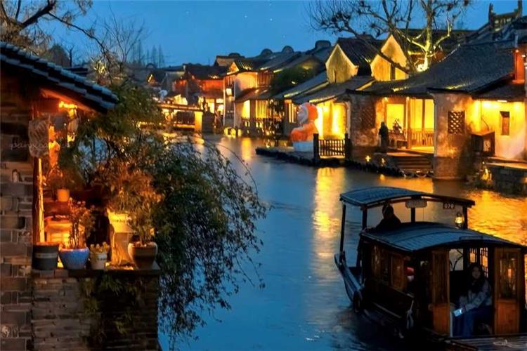 Illuminated Night Canal of Wuzhen Xizha Glowing lantern-lit ancient water town at dusk, wooden boat floating on reflective canal water in Wuzhen Xizha