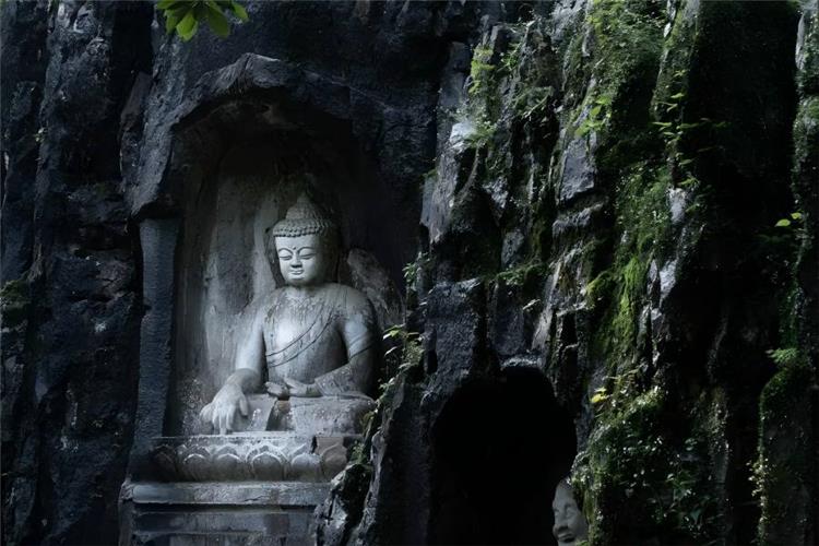Millennium Cliff Buddha Feilai Peak Weathered stone Buddha sculpture in Feilai Peak grotto, carved deep inside rugged dark cliff, green moss and wild plants covering rock walls, retaining primitive solemn charm of Southern Song Buddhist stone art