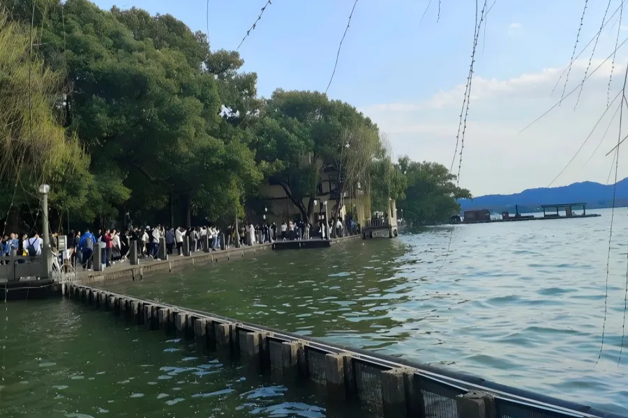 Stroll Along West Lake Lakeshore West Lake Lakeside in Hangzhou showing visitors wandering tree-lined causeway beside rippling lake waters