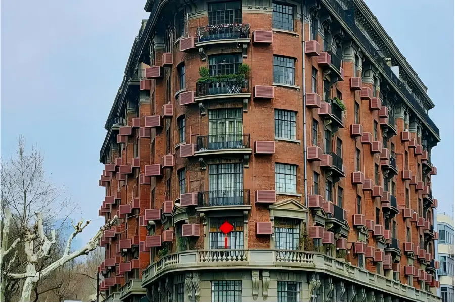 Century-old Normandie Apartments with red brick facade, standing at the crossroads shaded by lush plane trees