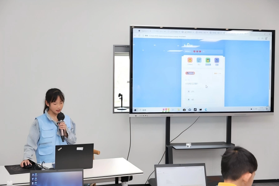 Students presenting study?tour project achievements Student giving speech with microphone, demonstrating AI project results on large screen