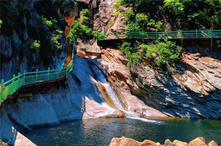 Waterfall and Cliff Boardwalk at Beijing Heilongtan Mountain waterfall dropping into green pool beside green?railed cliff boardwalk in Heilongtan canyon