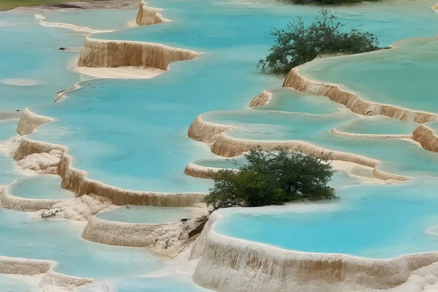 Layered mineral?deposit ponds shifting in turquoise and gold hues, ancient Huanglong Temple amid alpine mountain scenery