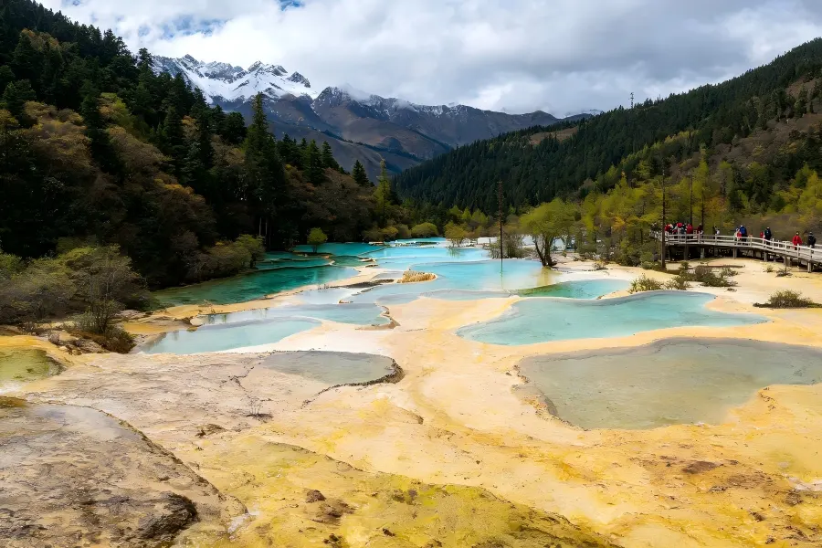 Huanglong Scenic Area in Aba tracing terraced shimmering calcite pools cascading down golden travertine slope backed by snow?capped Minshan mountain
