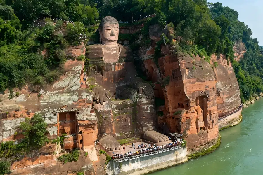Leshan Giant Buddha in Sichuan viewing grand Tang?dynasty cliff?carved Maitreya statue seated at river confluence, steep red sandstone cliff cloaked in green foliage