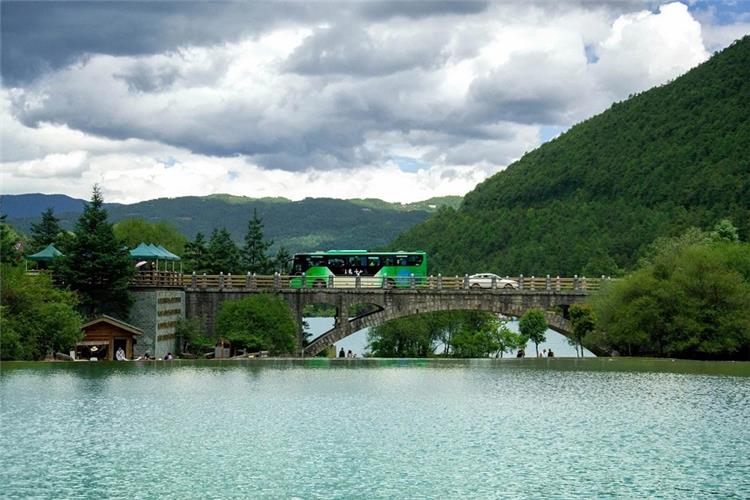 Blue Moon Valley Stone Arch Bridge, Jade Dragon Snow Mountain Tour bus crossing stone bridge over turquoise lake, green mountain scenery Lijiang