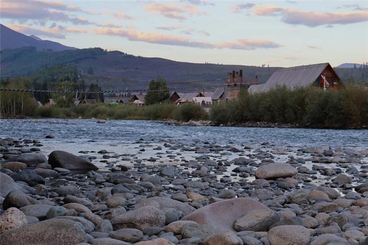 Twilight scenery of Hemu wooden log houses, rocky river bank and rolling hills in Altai Xinjiang