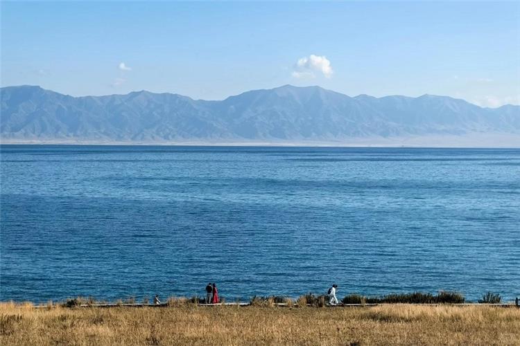 Panoramic view of Sayram Lake shoreline, visitors walking along trail, distant Tianshan mountain range Xinjiang