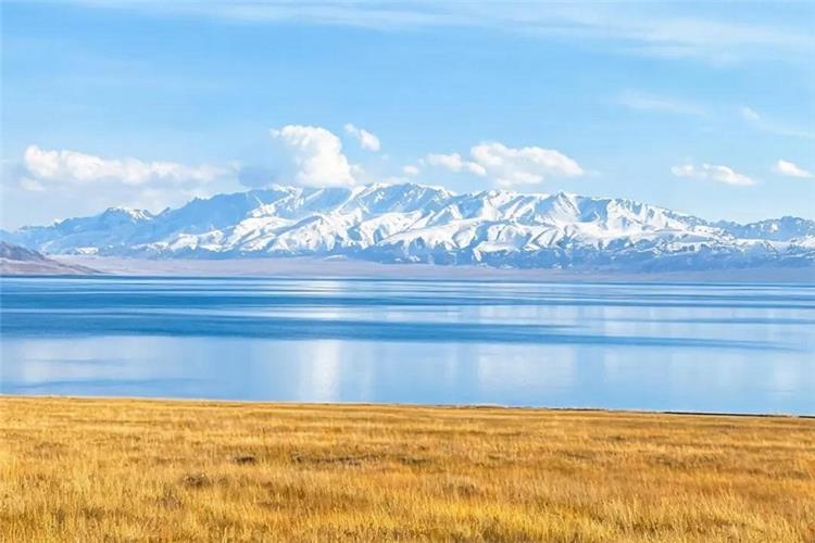 Panoramic view of Sayram Lake with blue water, snow mountain range and golden autumn grassland in Xinjiang China