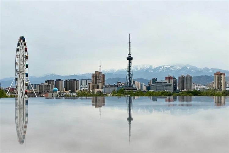 Bole cityscape reflected on mirror surface, ferris wheel and communication tower with distant snow mountains, Xinjiang