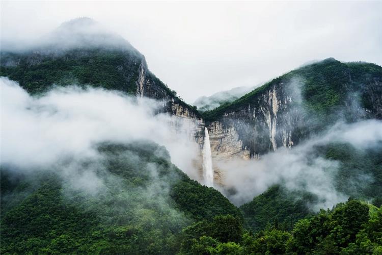 Misty Enshi Grand Canyon, towering cliff waterfall, green mountains wrapped in rolling white clouds