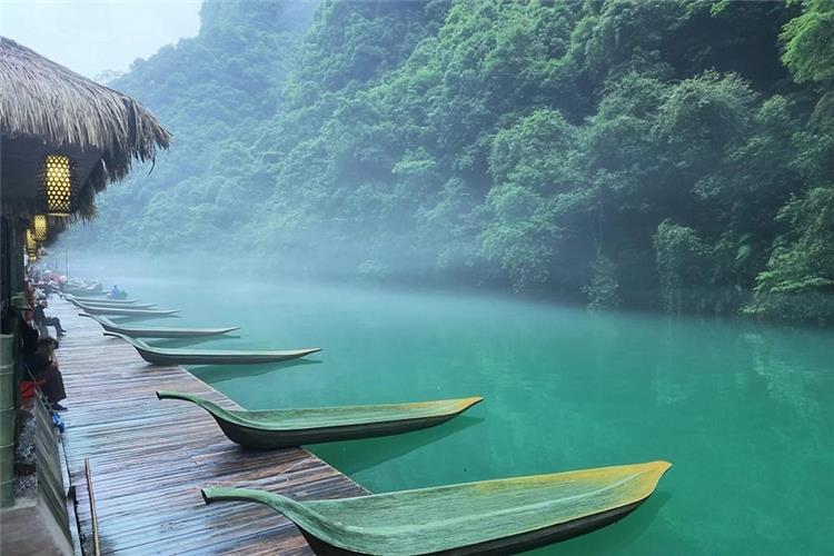 Wooden dock and slender boats on emerald river, morning mist floating over water