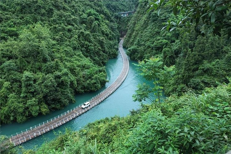 Aerial view of winding floating bridge over turquoise river, car driving on the water road surrounded by thick green mountains