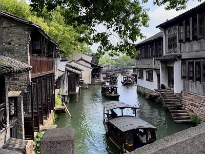 Traditional Jiangnan wooden houses lining calm water canals with wooden cruise boats, peaceful daytime scenery of Wuzhen Xizha water town