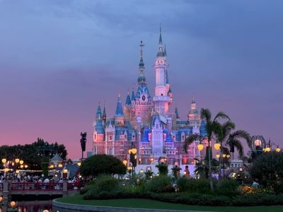 Twilight view of Shanghai Disneyland fairy-tale castle lit up with pink and purple glow.