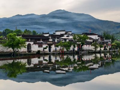 Scenic view of Hongcun Village Anhui, white Huizhou architecture reflected in calm lake with misty mountains backdrop