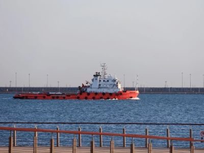 Red and white vessel cruising over blue water at Tianjin Port, pier scenery in foreground