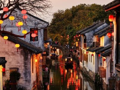 Glowing red and yellow lanterns, black-awning boat on reflective water, ancient white wall houses at Zhouzhuang Ancient Town in Suzhou