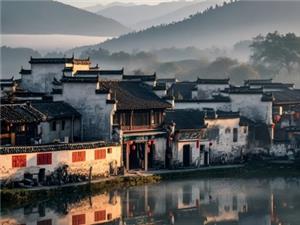 Classic white wall black tile Huizhou architecture by calm lake, mountain mist background, ancient Hui-style houses with perfect water reflection at dawn