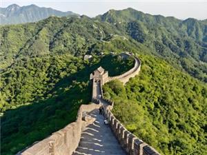 Mutianyu Great Wall with steep stone steps and watchtower, snaking over lush green forested hills under clear sky, iconic Beijing landmark
