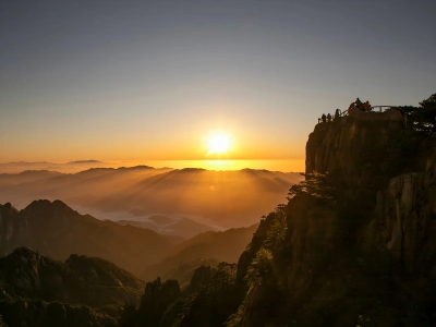 Golden sunrise above layered mountain ridges and sea of clouds in Huangshan, tourists standing on cliff viewing platform