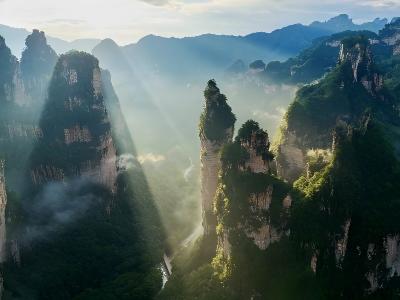 Mist-shrouded Zhangjiajie stone peaks with golden sunbeams through mountain valleys, iconic Hunan natural scenery