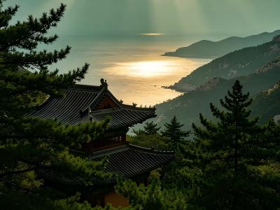 Sunrise over the sea from Laoshan Mountain with traditional Taoist temple rooftops in Qingdao, China