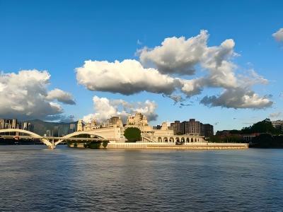 Min River scenery showing the peaceful riverside, historic city architecture, bridge, and blue sky with floating clouds