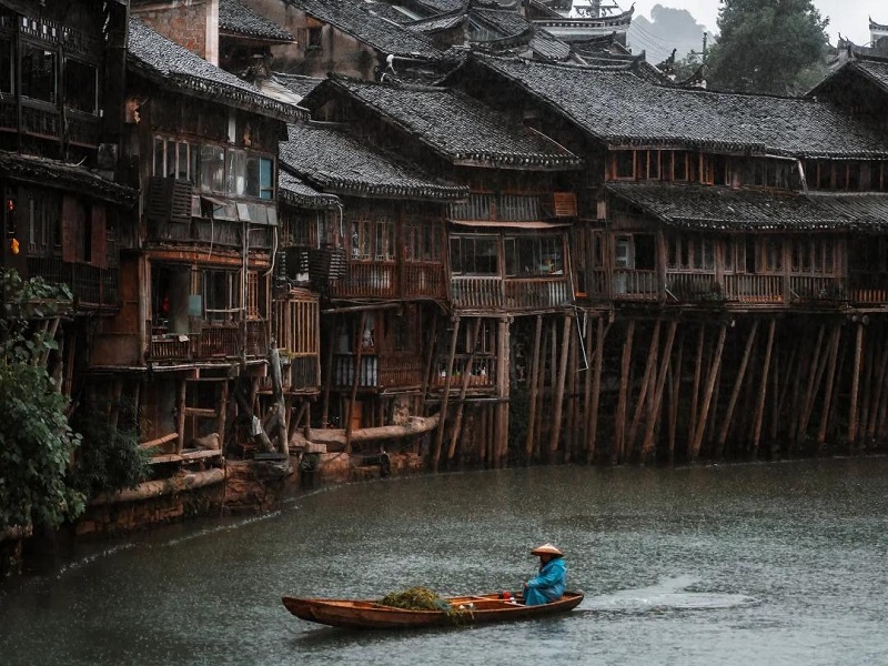 Moody rainy view of Fenghuang Ancient Town with stilt buildings and boat on Tuojiang River, Hunan China