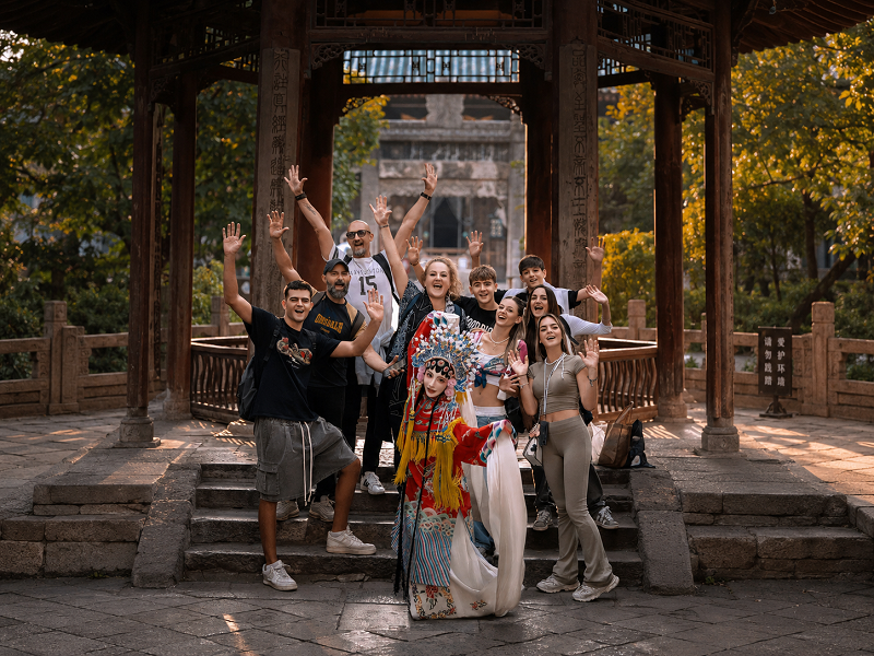 Foreign travel group posing with Peking Opera artist at ancient pavilion