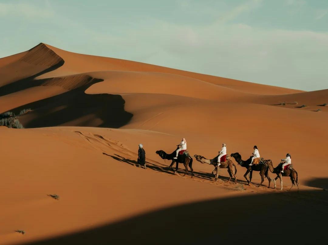Taklamakan Desert in Xinjiang with golden sand dunes, oasis scenery, blue water, and camel riders in the desert