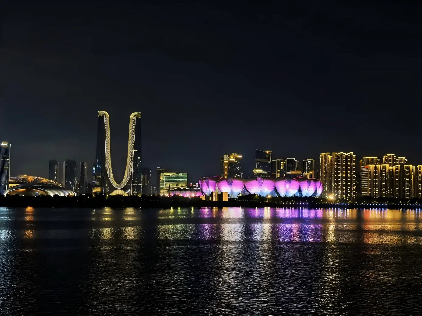 Illuminated Grand Lotus stadium and twin towers beside Qiantang River at night